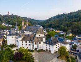 Luftaufnahme von Schloss Clervaux in Luxemburg, umgeben von Wald und Stadtgebäuden.